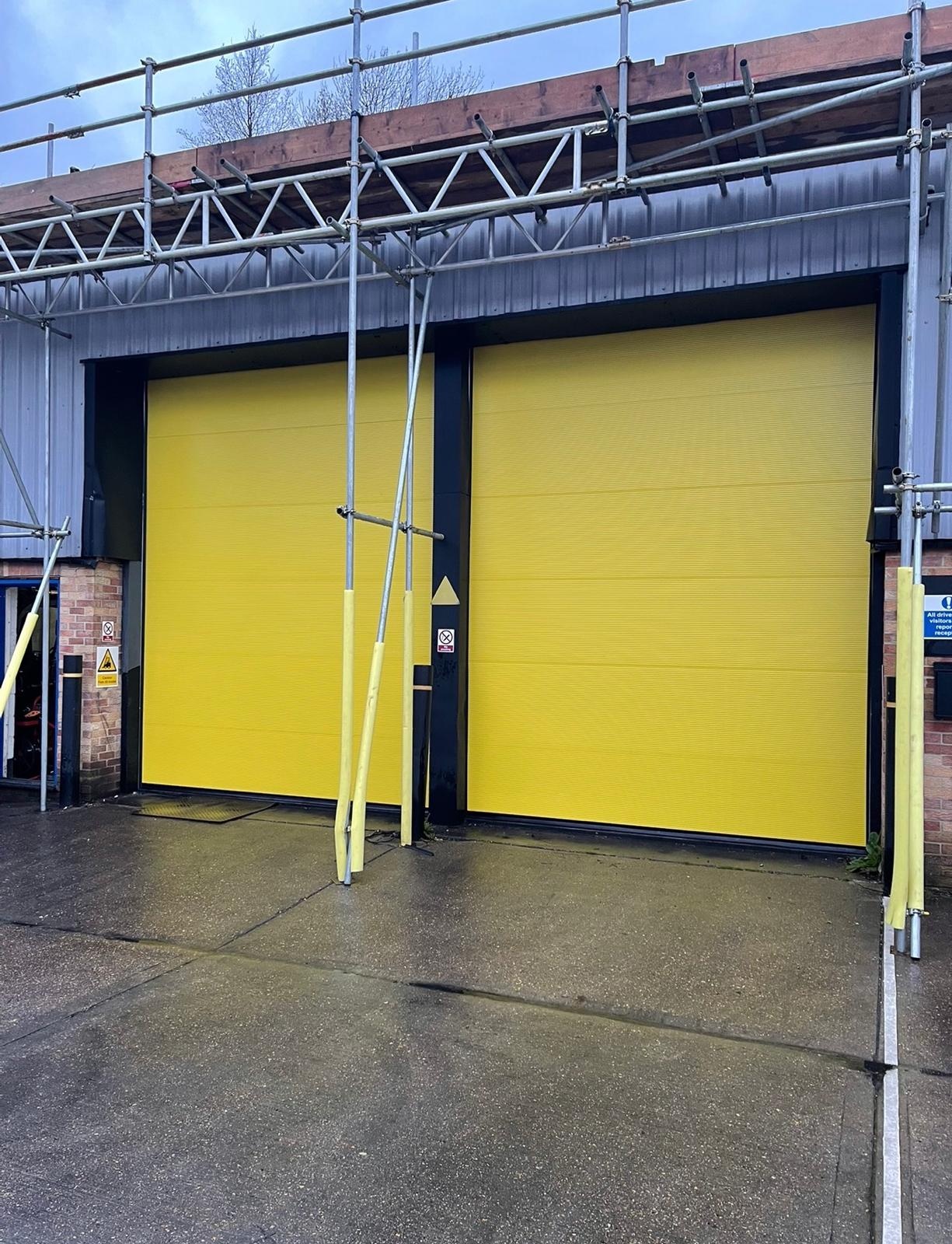 Yellow sectional overhead doors during installation behind scaffolding