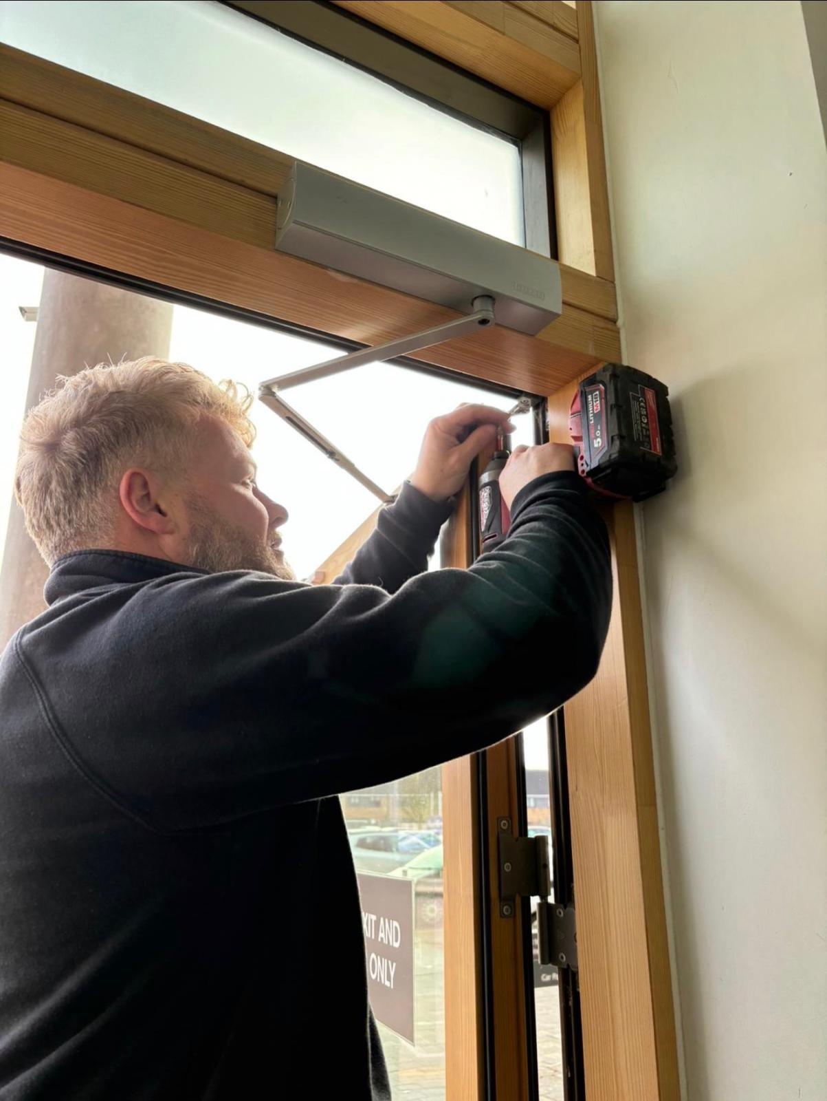 Engineer fitting a door closer during a commercial door installation