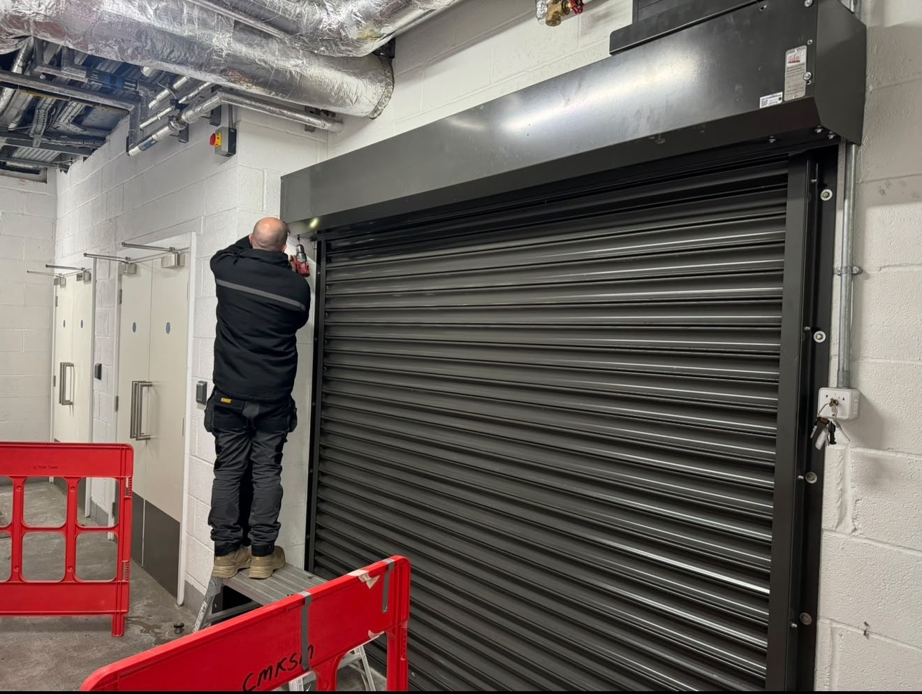 Engineer servicing the casing of a grey roller shutter door